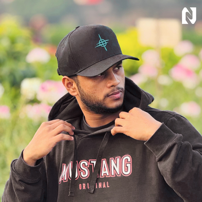 Man wearing a black cap and hoodie with 'Mustang Original' text, standing in a blurred outdoor setting.