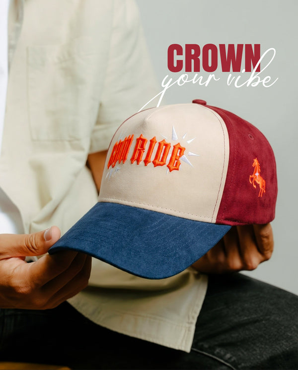 A person holds a two-tone baseball cap with a cream front panel, dark red side panels, and a blue denim brim. The front panel features the text 'COW RIDE' in orange with a white starburst, and the side panel has an orange embroidered horse logo.