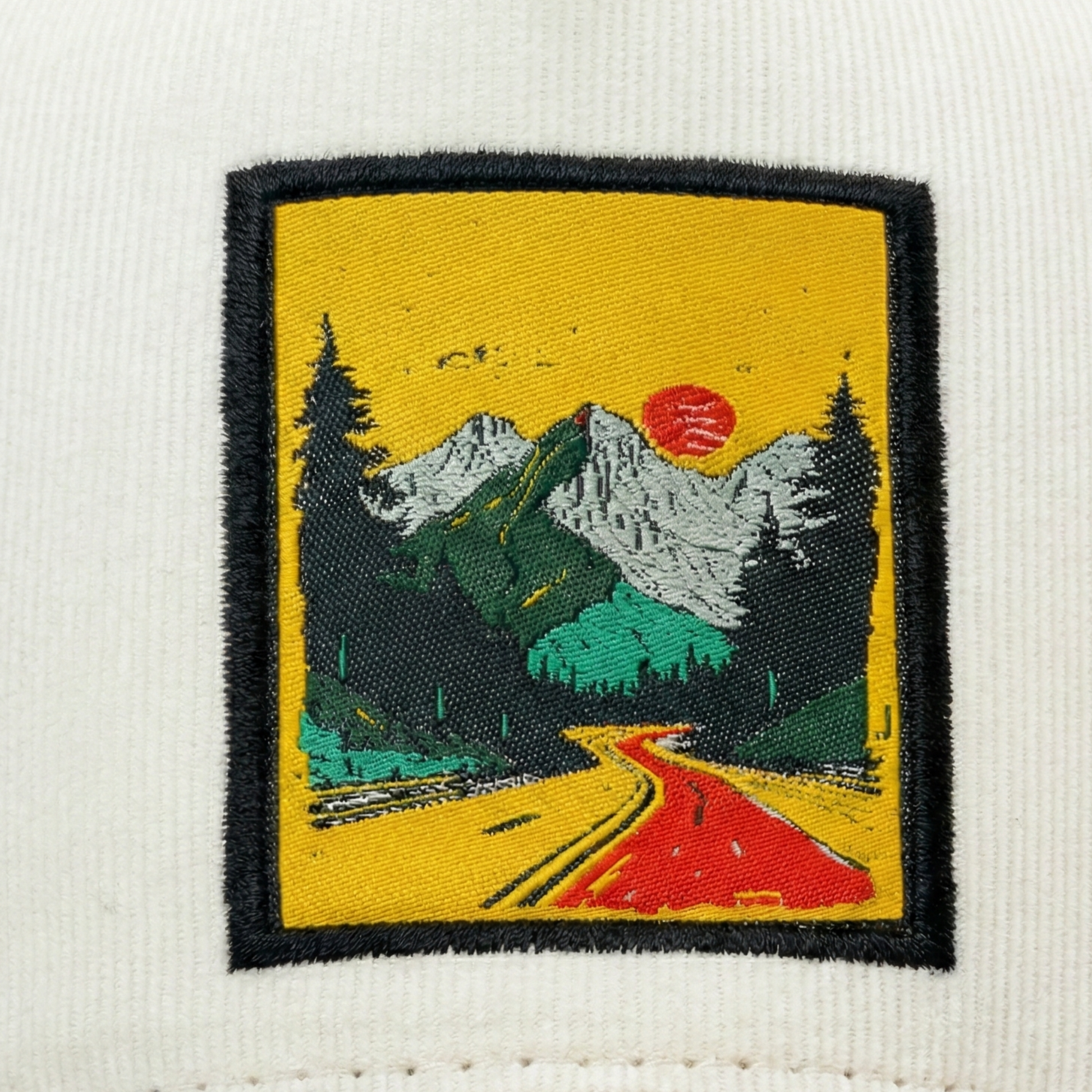 Embroidered patch of a mountain landscape with a road and trees on a white fabric background